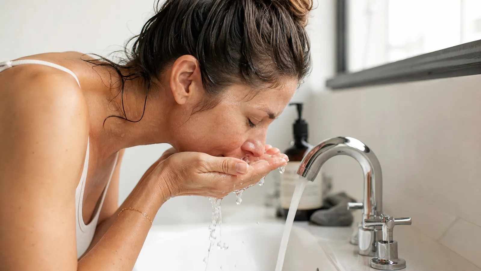 Woman gently washing her face at a bathroom sink in soft morning light