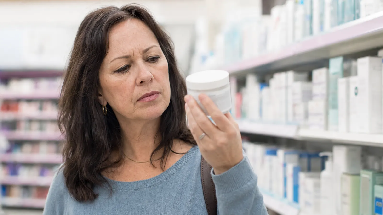 Woman standing in a drugstore skincare aisle reading the back label of a retinol jar